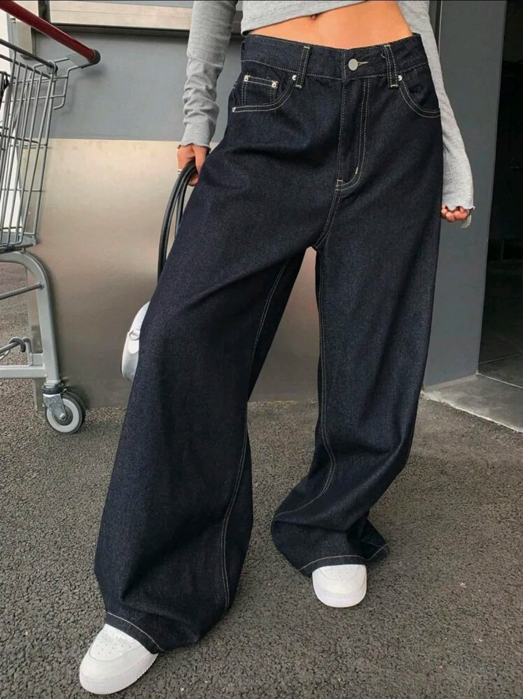 Person wearing wide-leg dark blue jeans with a blurred background