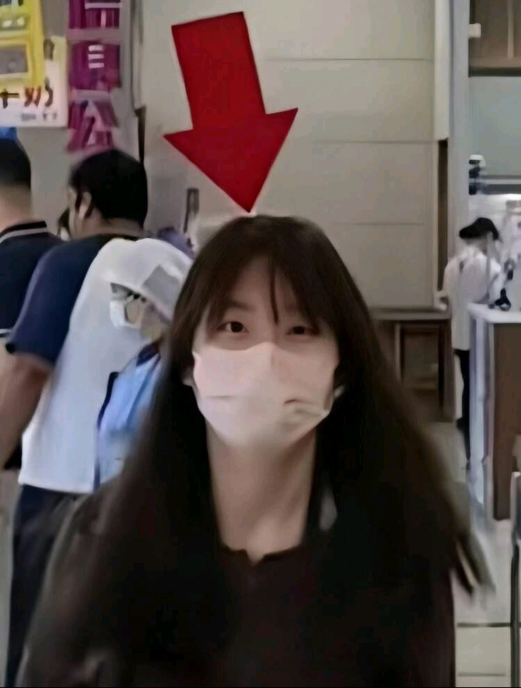 Woman wearing a face mask in a public setting with a red arrow pointing downwards on a wall.