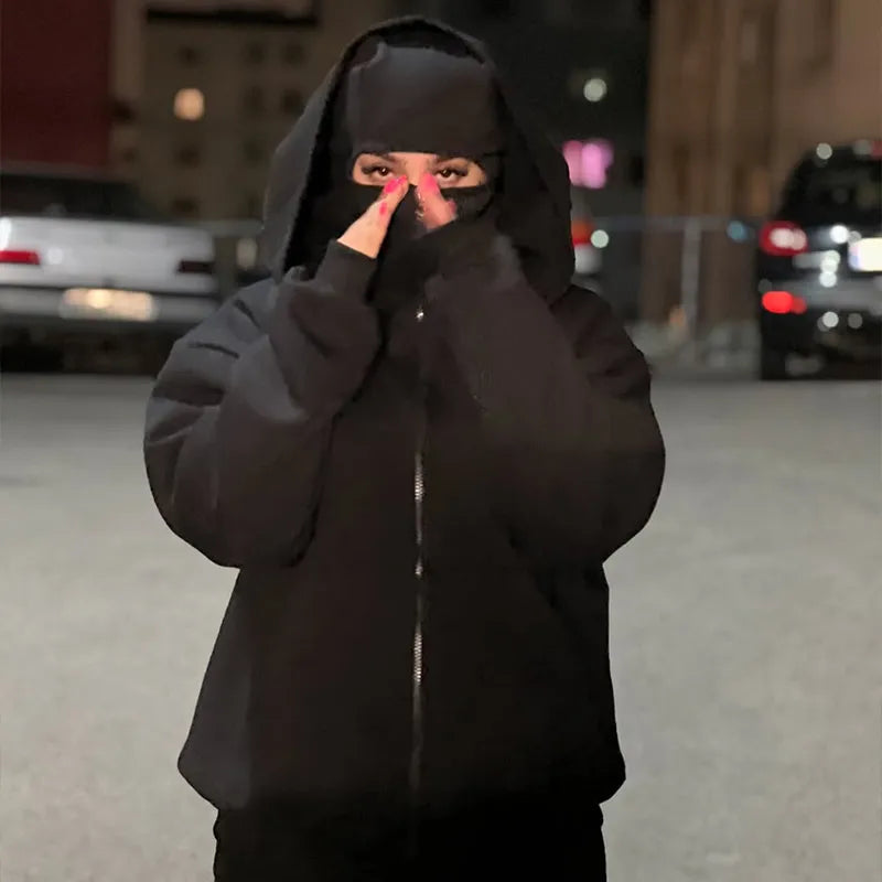 Person wearing a black hoodie and mask in an urban setting