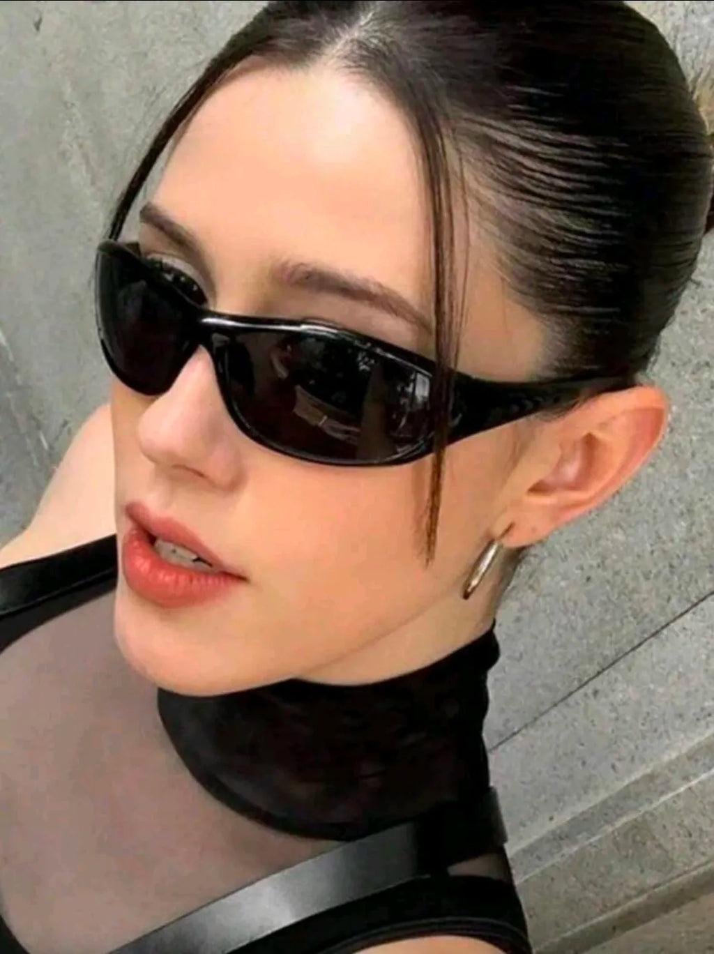 Person wearing black sunglasses and a black outfit against a gray background