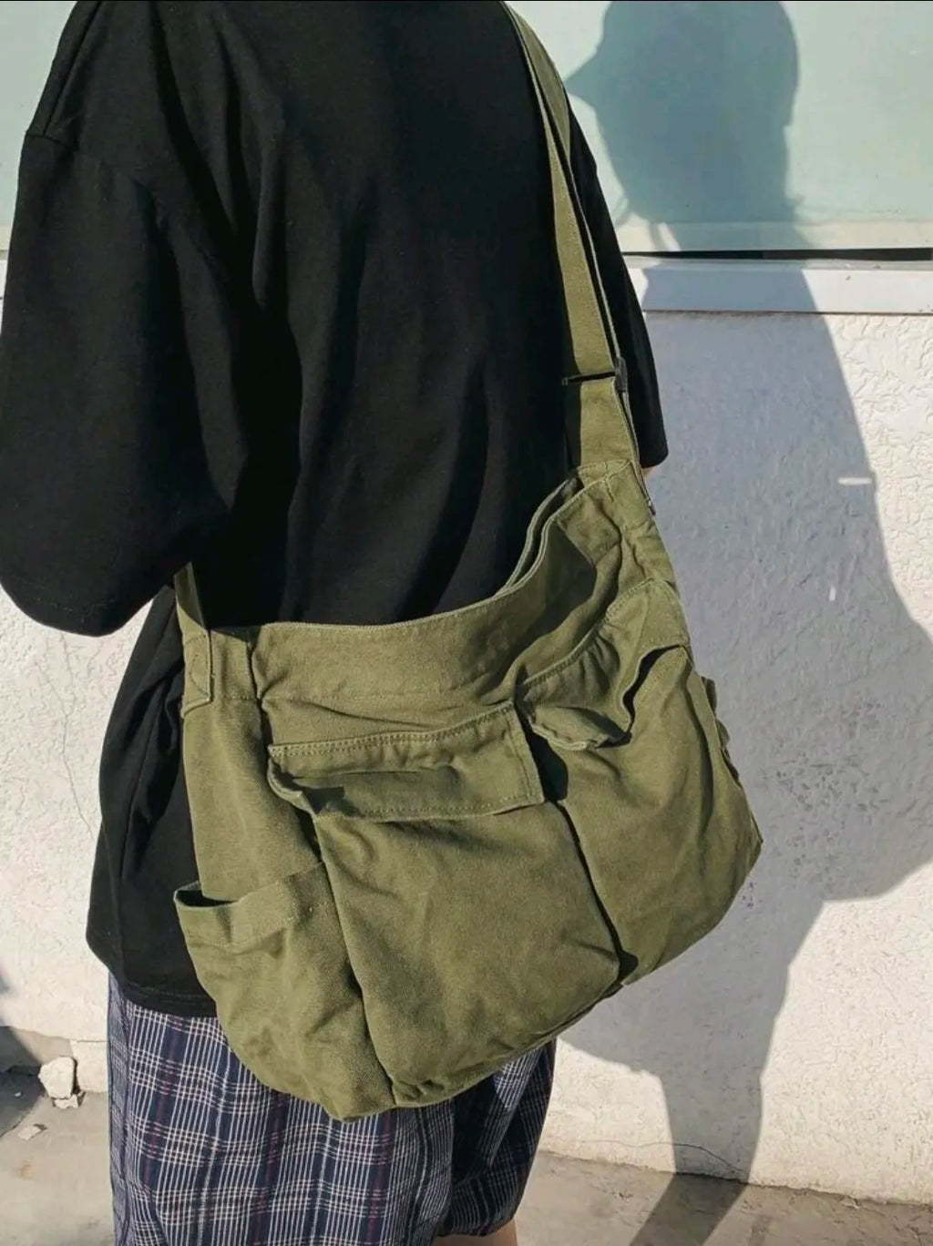 Person wearing a green bag over one shoulder against a light-colored wall.