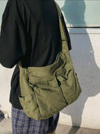 Person wearing a green bag over one shoulder against a light-colored wall.