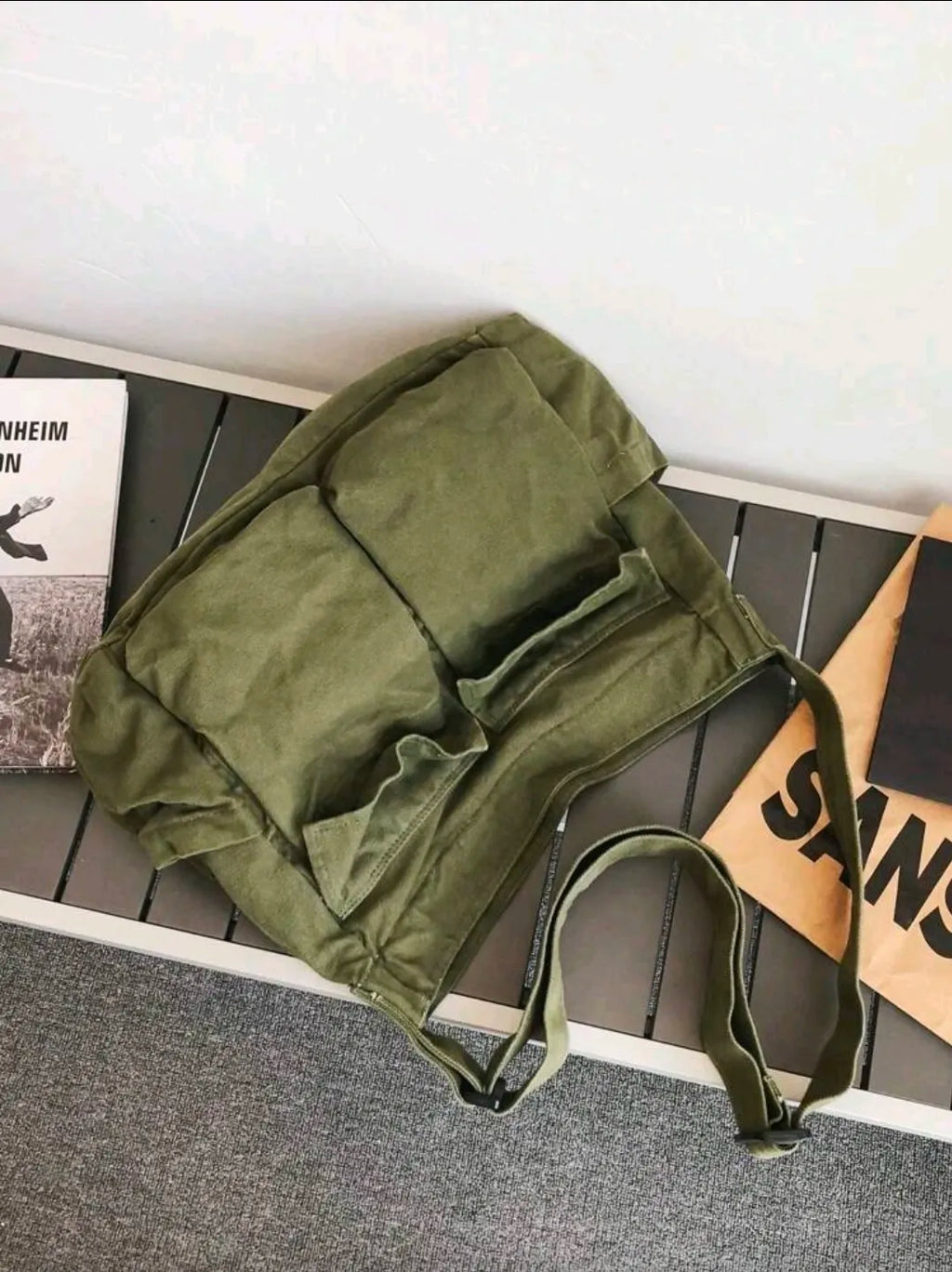 Green bag on a wooden surface with a book and a cardboard box in the background