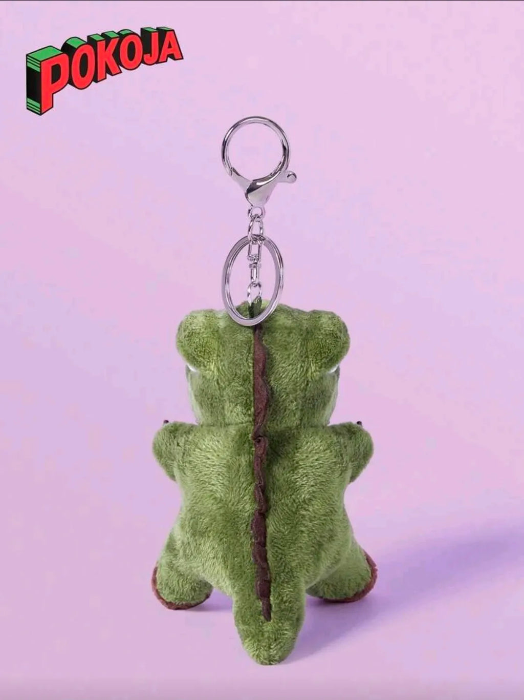Green plush keychain with a stick on a light purple background, featuring the Pokoja brand.