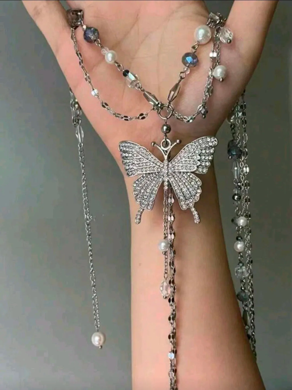 Butterfly-shaped jewelry with pearl accents on a hand against a neutral background
