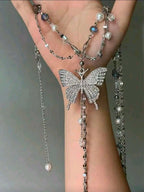 Butterfly-shaped jewelry with pearl accents on a hand against a neutral background